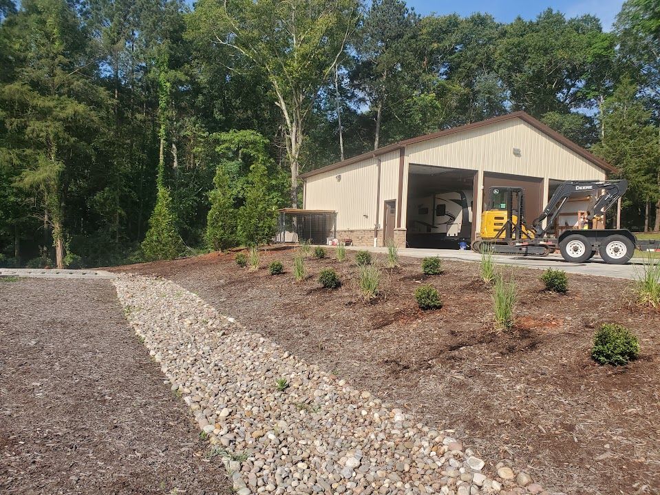 newly installed river rock landscape next to a large garage with a bulldozer parked in front of it 