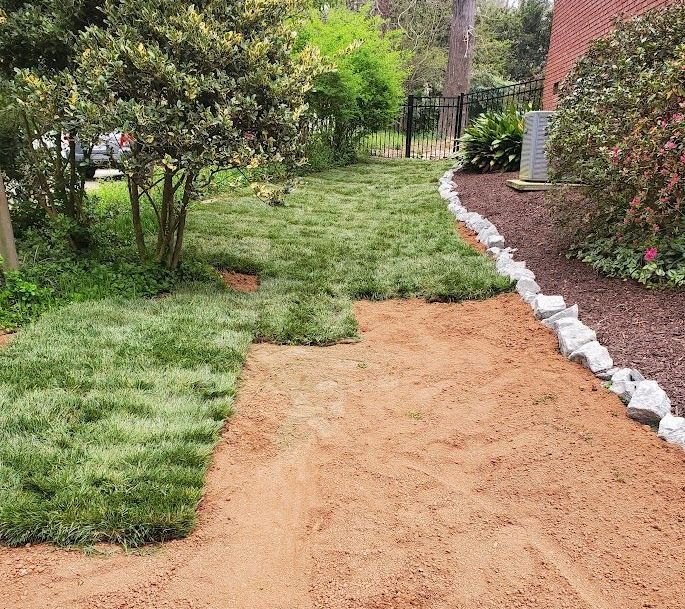 fresh sod being installed in dirt leading to a lush green yard with a brick building in the background
