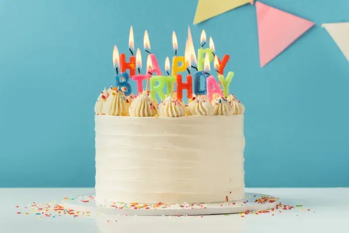 Birthday cakes with pastel frosting, candles, and decorations on a table.