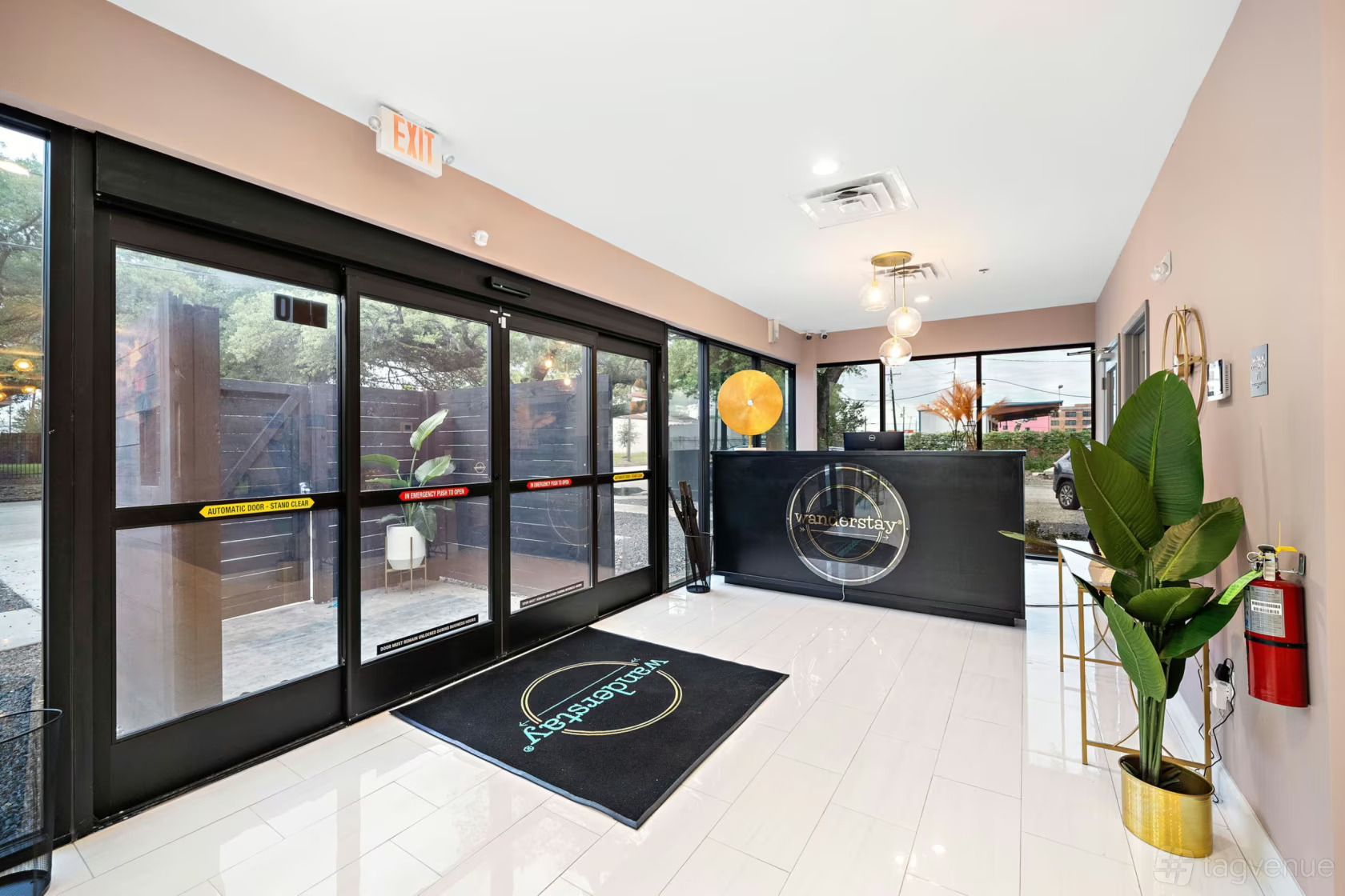 Entryway with sliding glass doors, black reception desk, potted plant, exit sign, and a logo rug.