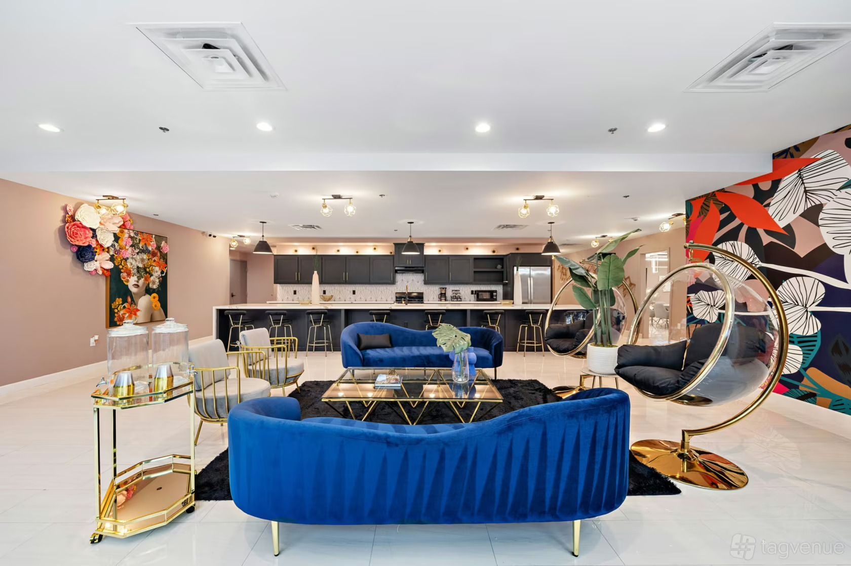 Luxurious lounge with blue velvet sofas, gold chairs, and vibrant mural. Large windows overlook a patio.