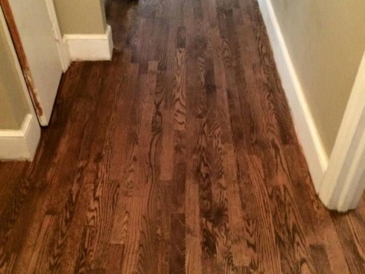 A man is walking down a hallway with hardwood floors.