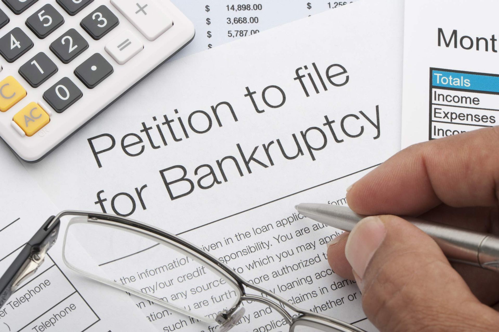 Close up of bankruptcy petition with calculator and writing hand.