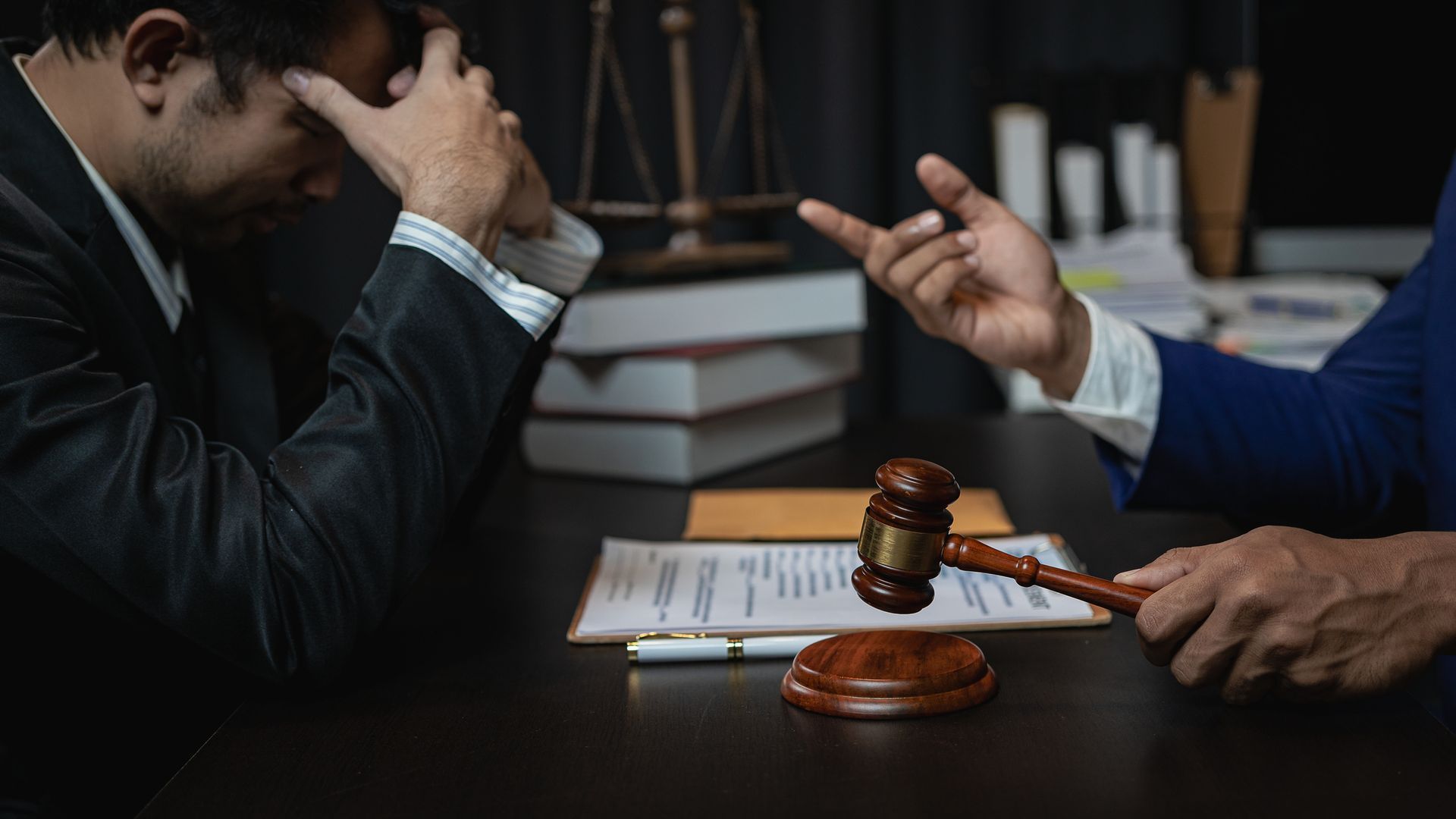 A lawyer and client speak over a table with forms and a gavel. A lawyer and client speak over a table with forms and a gavel.