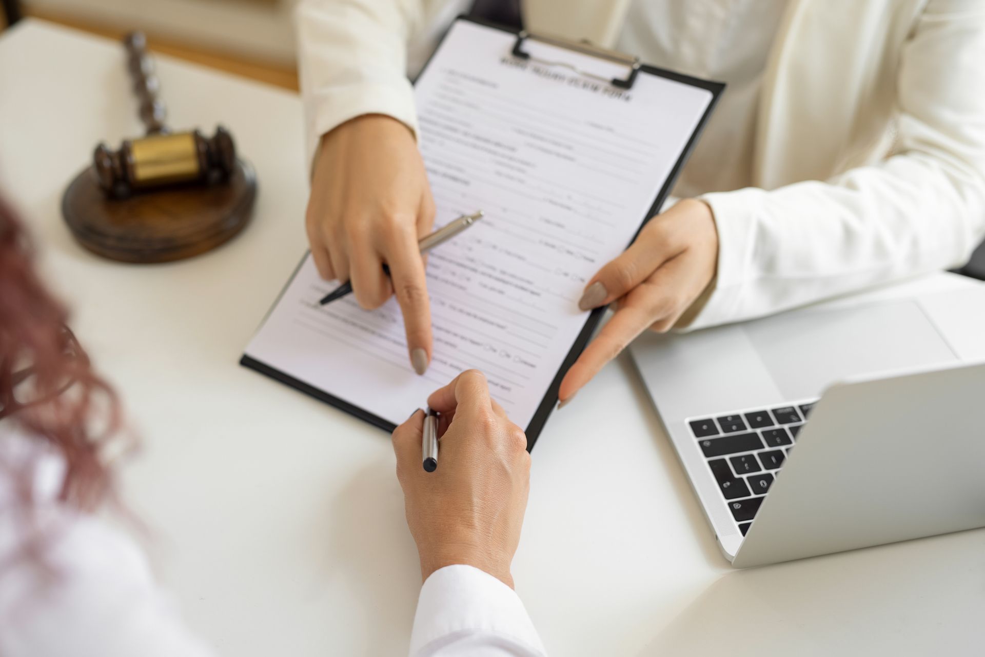 A lawyer, while holding a file on a clipboard, points to in front of their client. A lawyer, while holding a file on a clipboard, points to in front of their client.