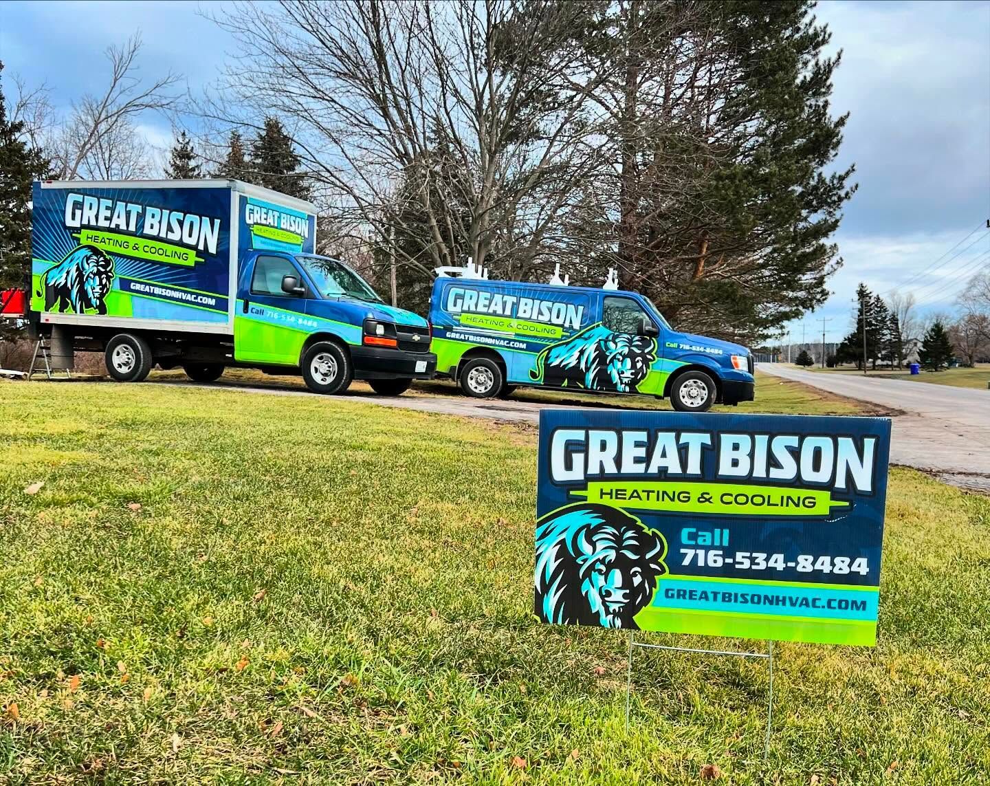 Two Great Bison Heating & Cooling trucks with a sign. A blue and green color scheme on a grassy field.