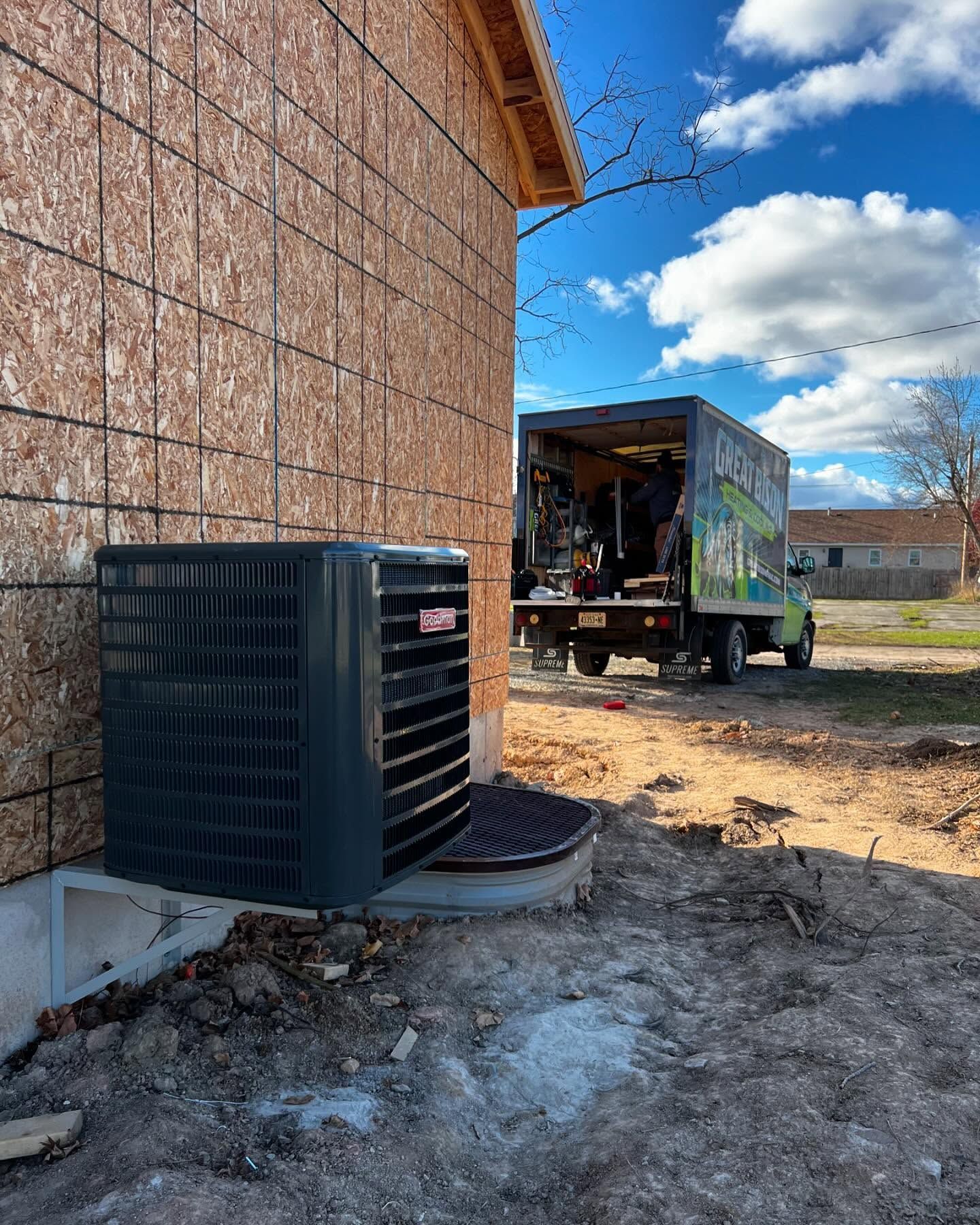 HVAC unit installed near a house under construction; a work truck parked nearby.