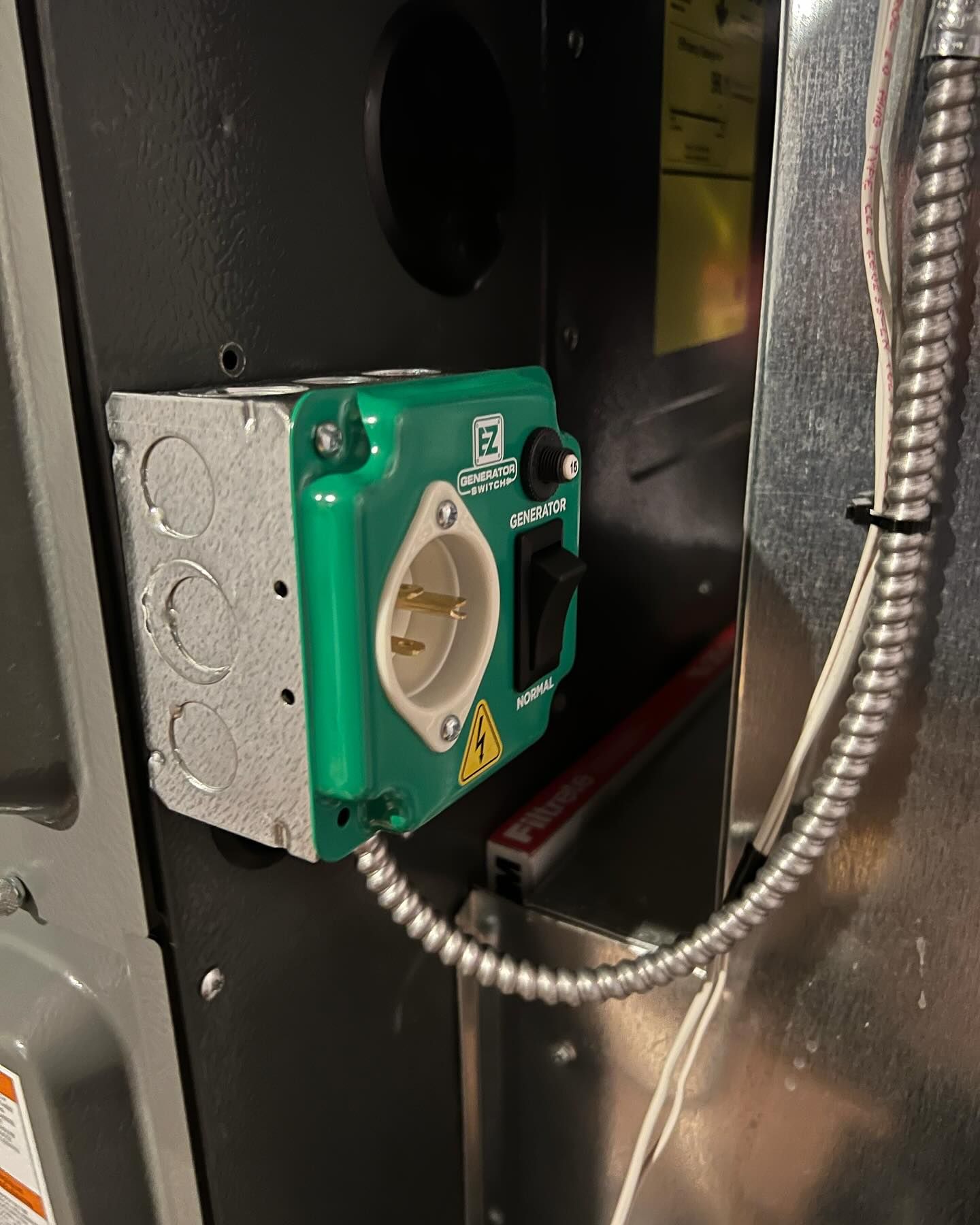 Green electrical outlet box mounted on a metal surface with an on/off switch and a flex conduit cable.