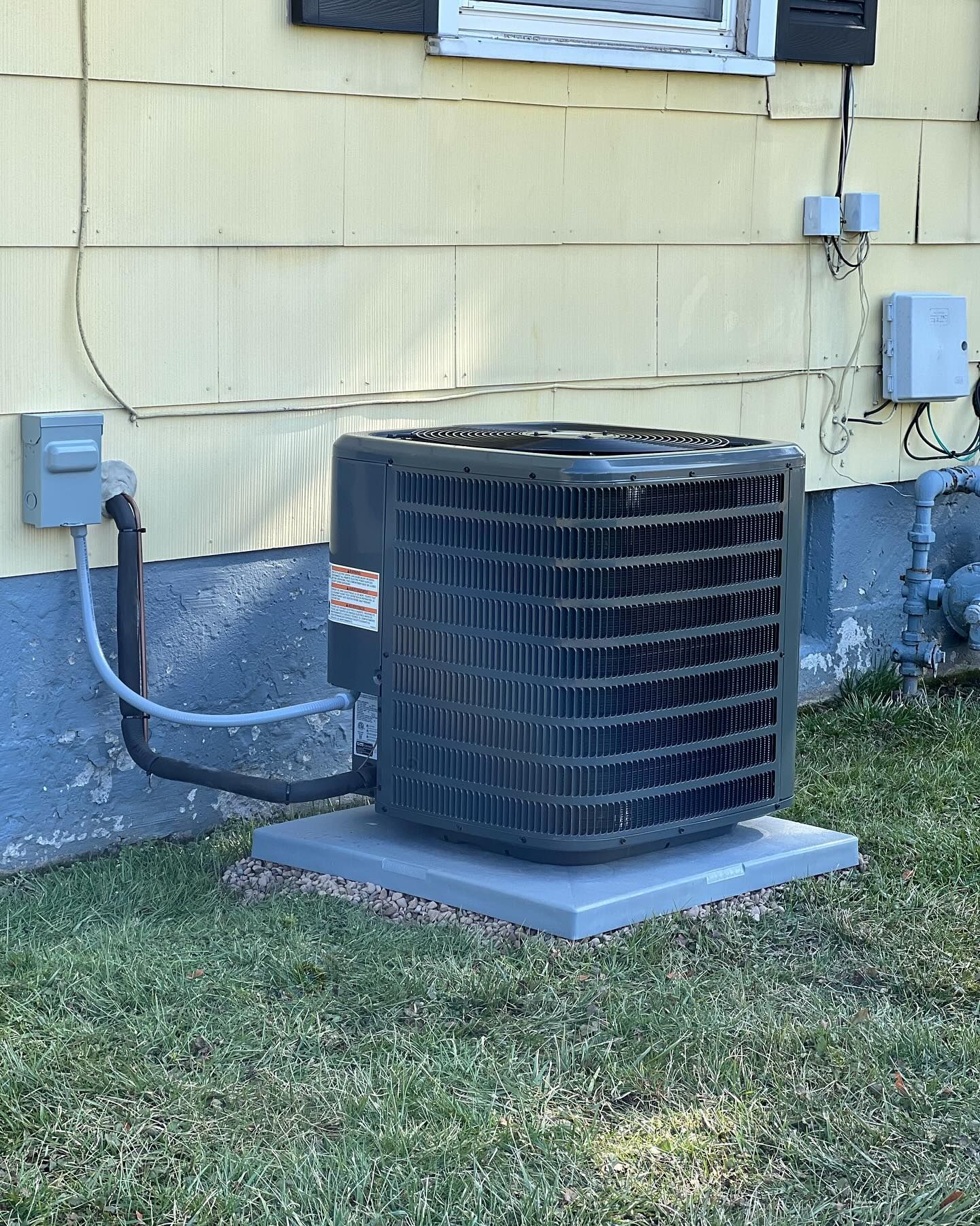 Air conditioning unit outside a yellow house on a concrete pad in the grass.