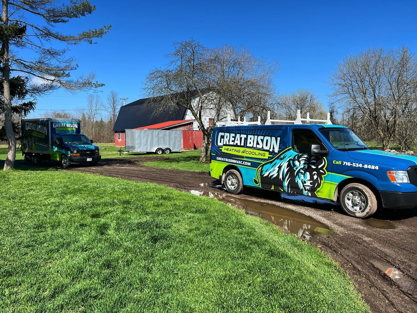 Two green and blue Great Bison service vans parked on a muddy path near a red barn.