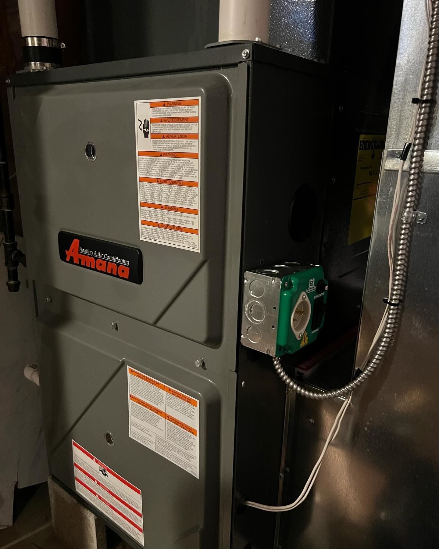 An Amana furnace in a utility room; gray and black with a green motor.