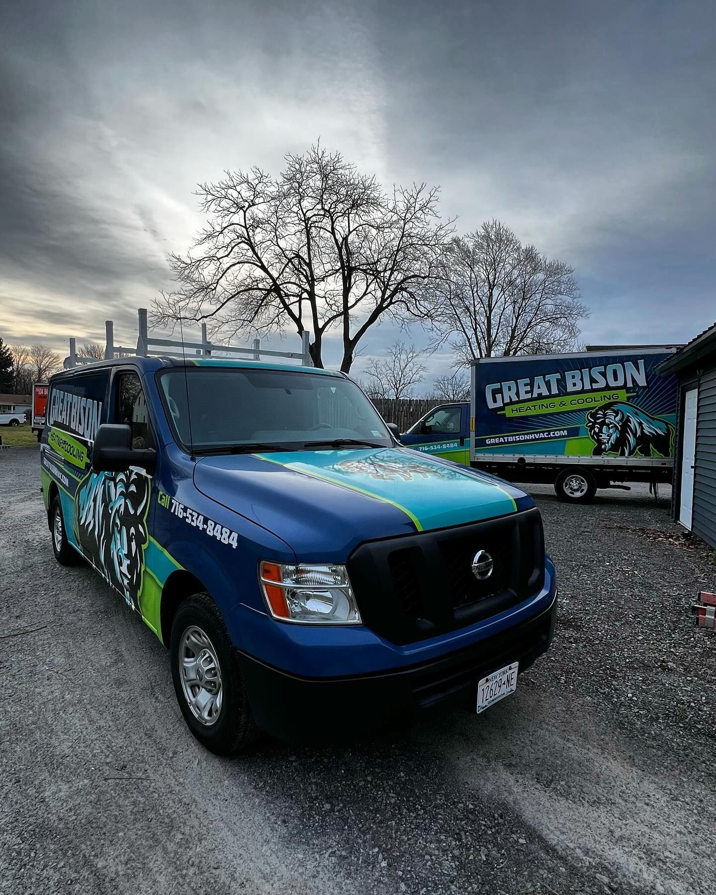Two Great Bison trucks, blue, green, and black, parked outside under a cloudy sky.