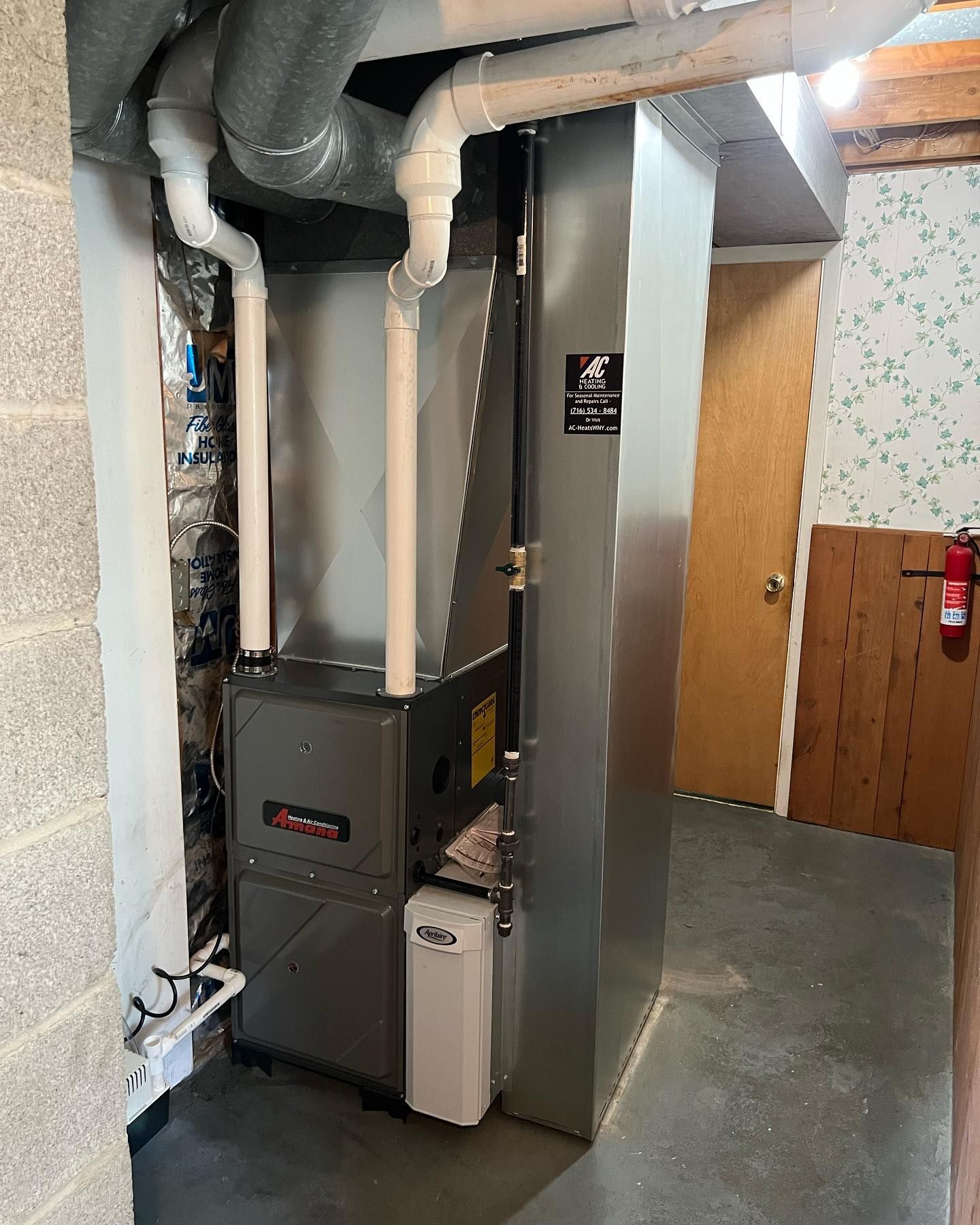 Furnace in a basement room with ductwork and humidifier. Door and fire extinguisher are also visible.