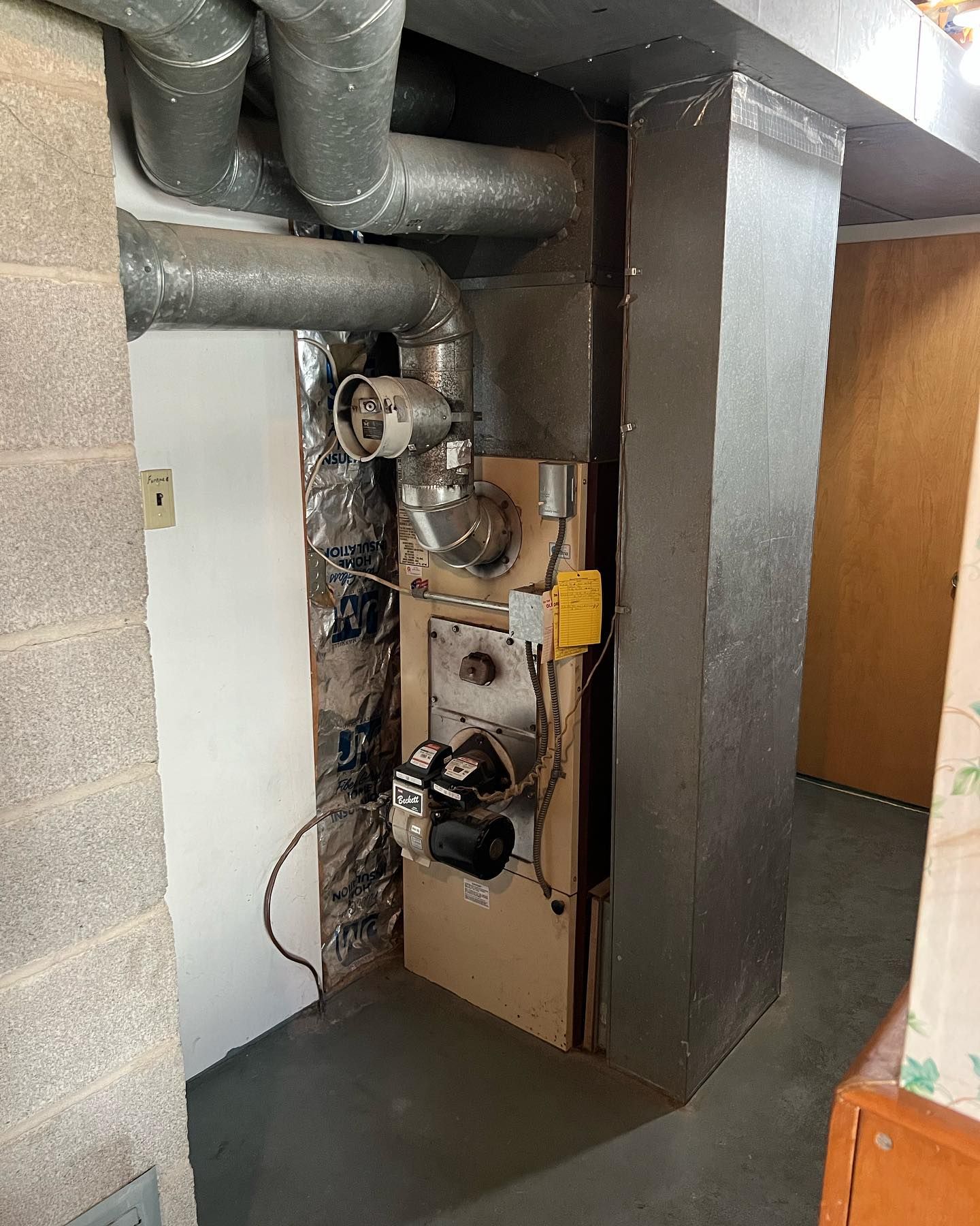 Furnace in a basement alcove with ductwork, a door, and cinder block wall.