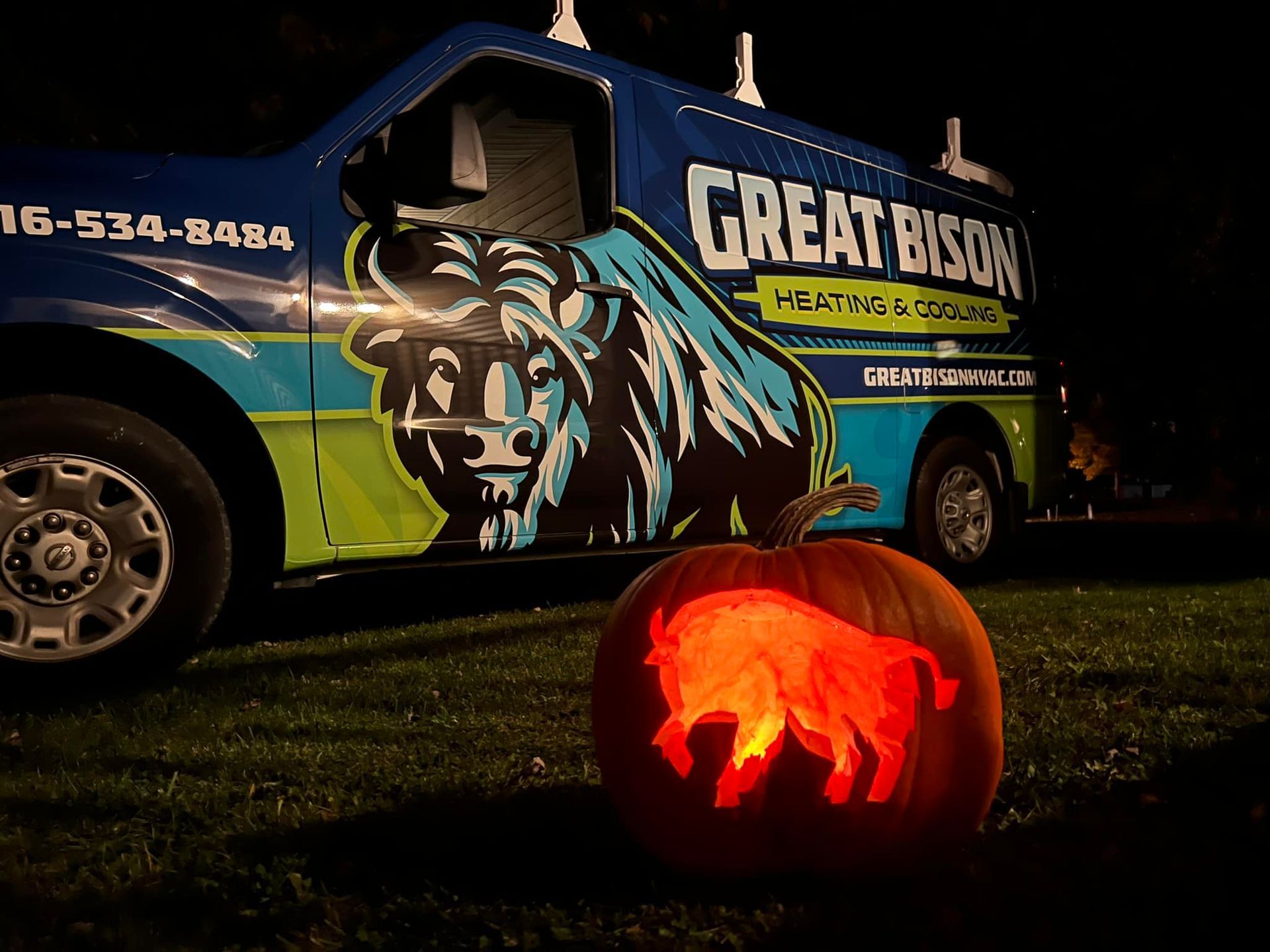 Pumpkin carved with bison logo glows in front of Great Bison Heating & Cooling truck at night.