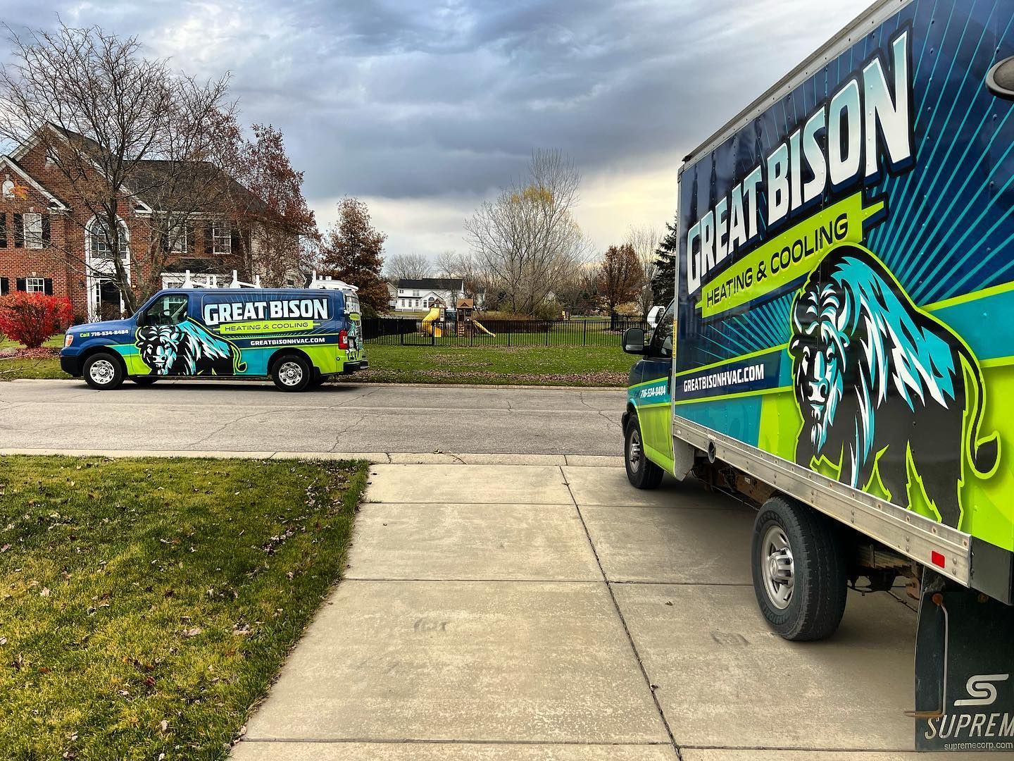 Two Great Bison Heating & Cooling trucks parked on a street in front of a house.
