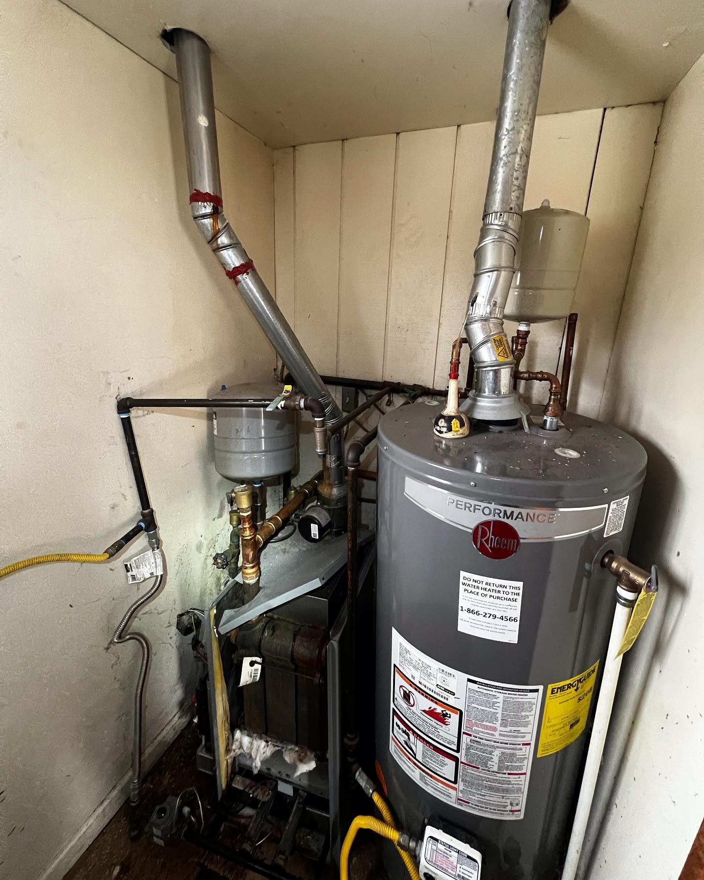 Two water heaters in a utility closet with ventilation pipes. One is tall, gray, and cylindrical.