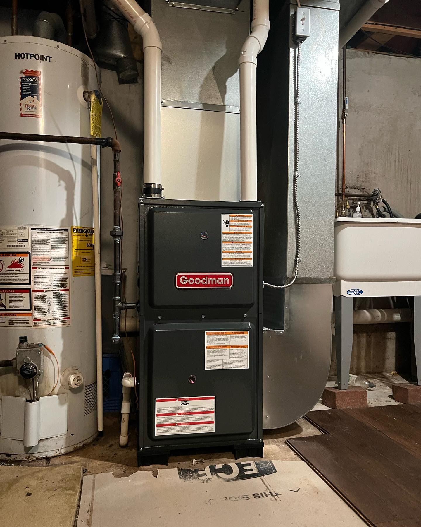 A Goodman furnace in a basement next to a water heater and laundry sink.
