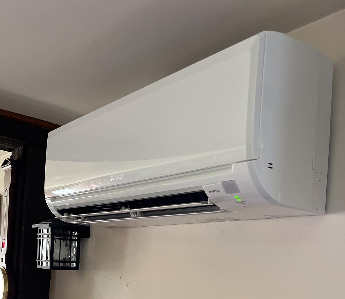White air conditioning unit mounted on a light-colored wall. A black wall fixture is below.