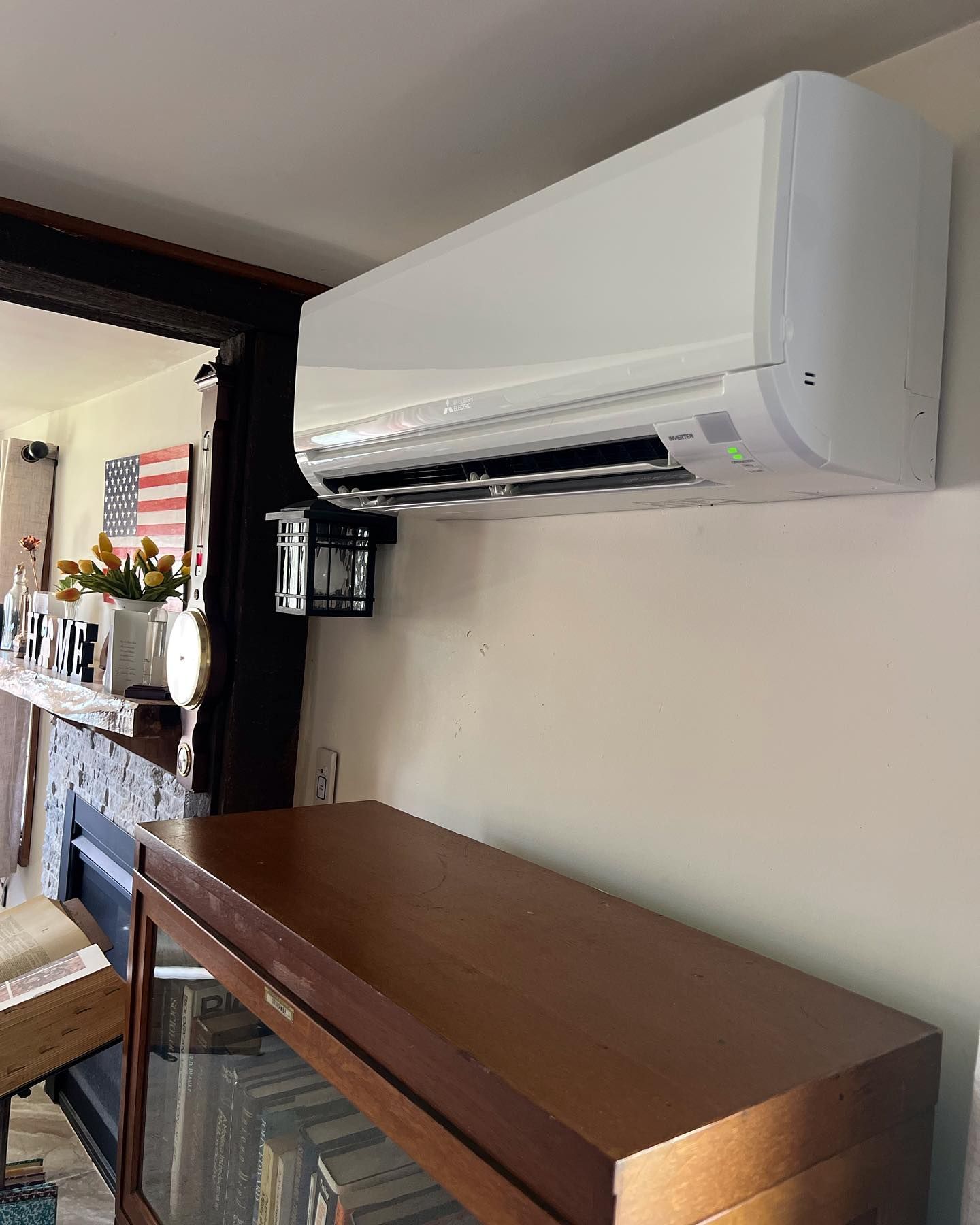 White wall-mounted air conditioner above a brown cabinet, interior shot with American flag in the background.