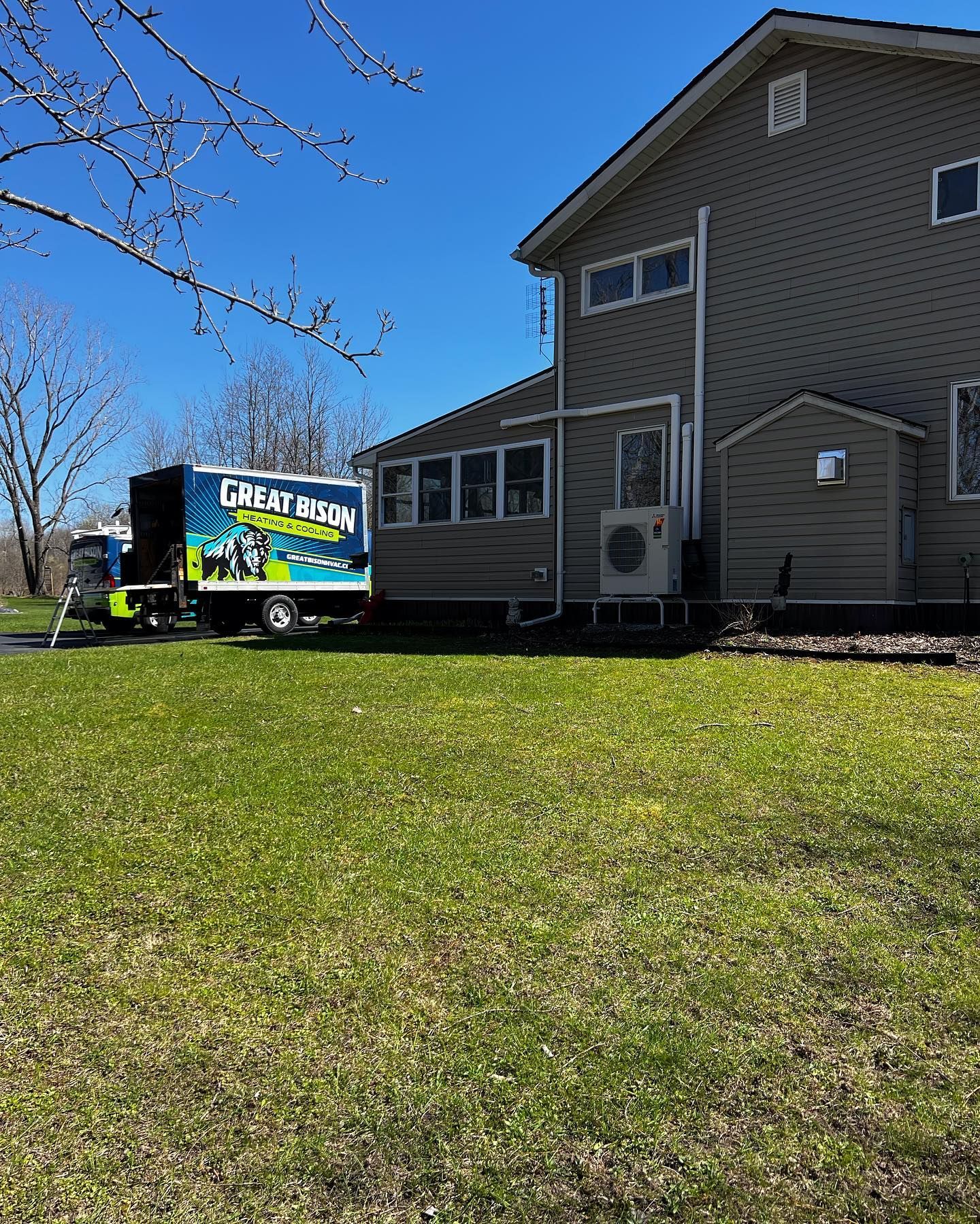 Truck from Great Bison Screen & Door beside a house on a sunny day. Green grass and blue sky.