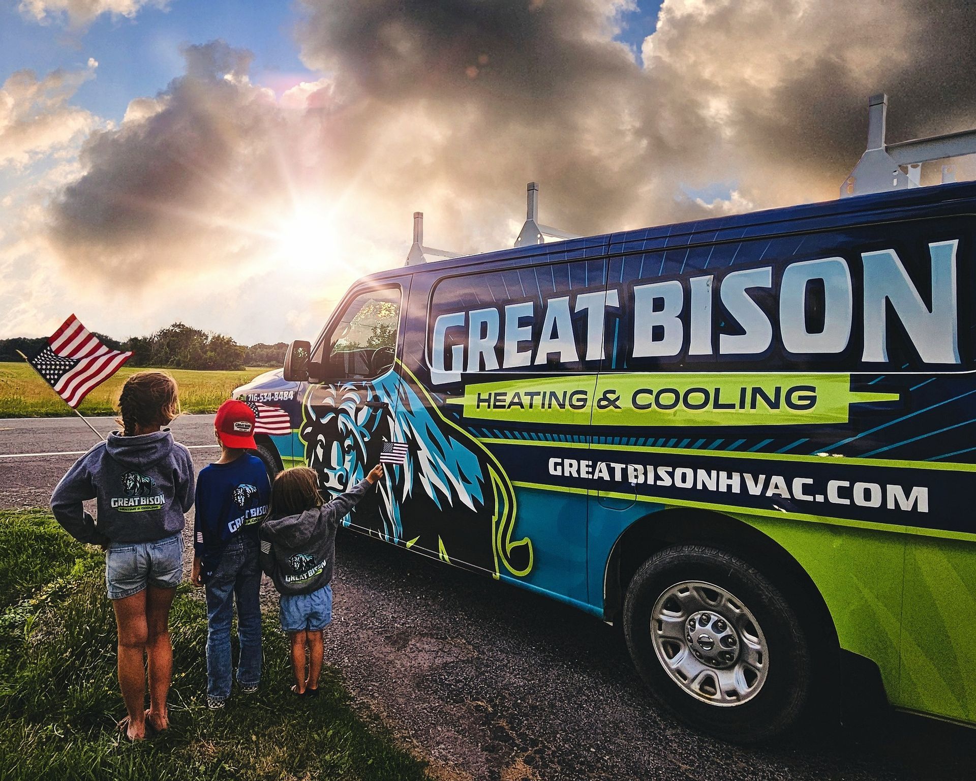 Children admire a Great Bison Heating & Cooling van with an American flag under a sunset.