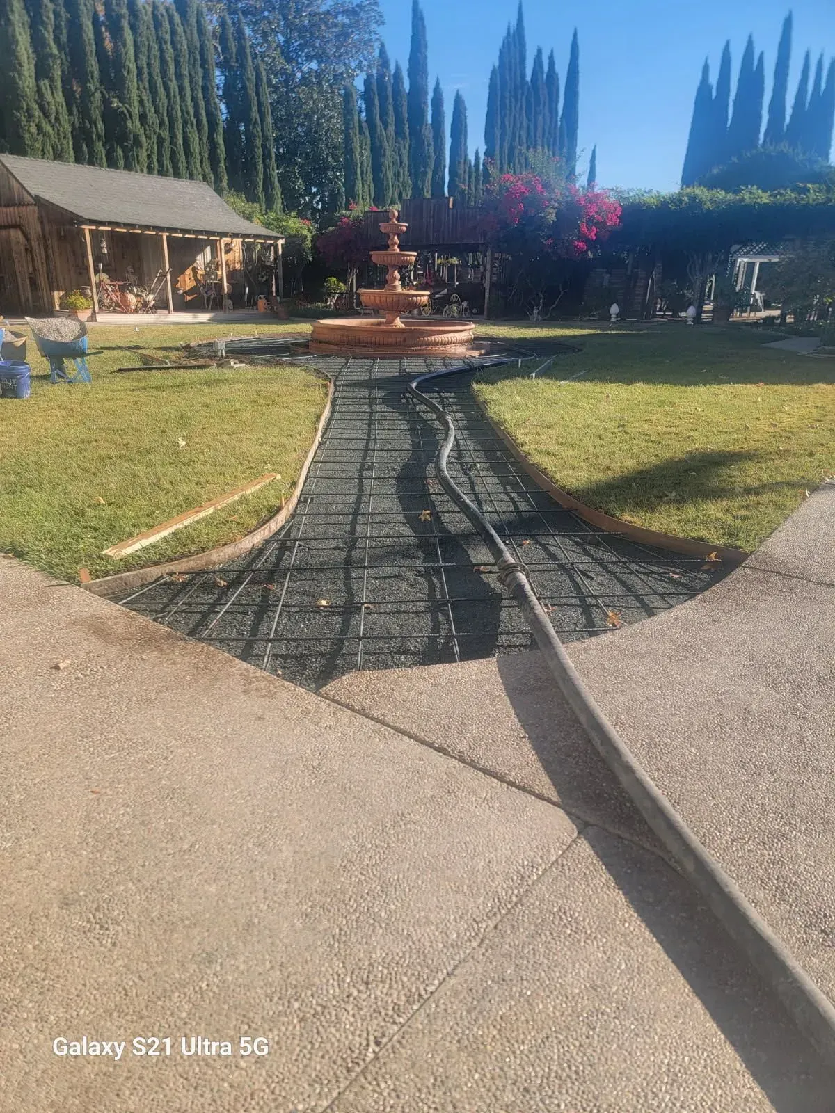 A concrete walkway is being built in a yard next to a fountain.