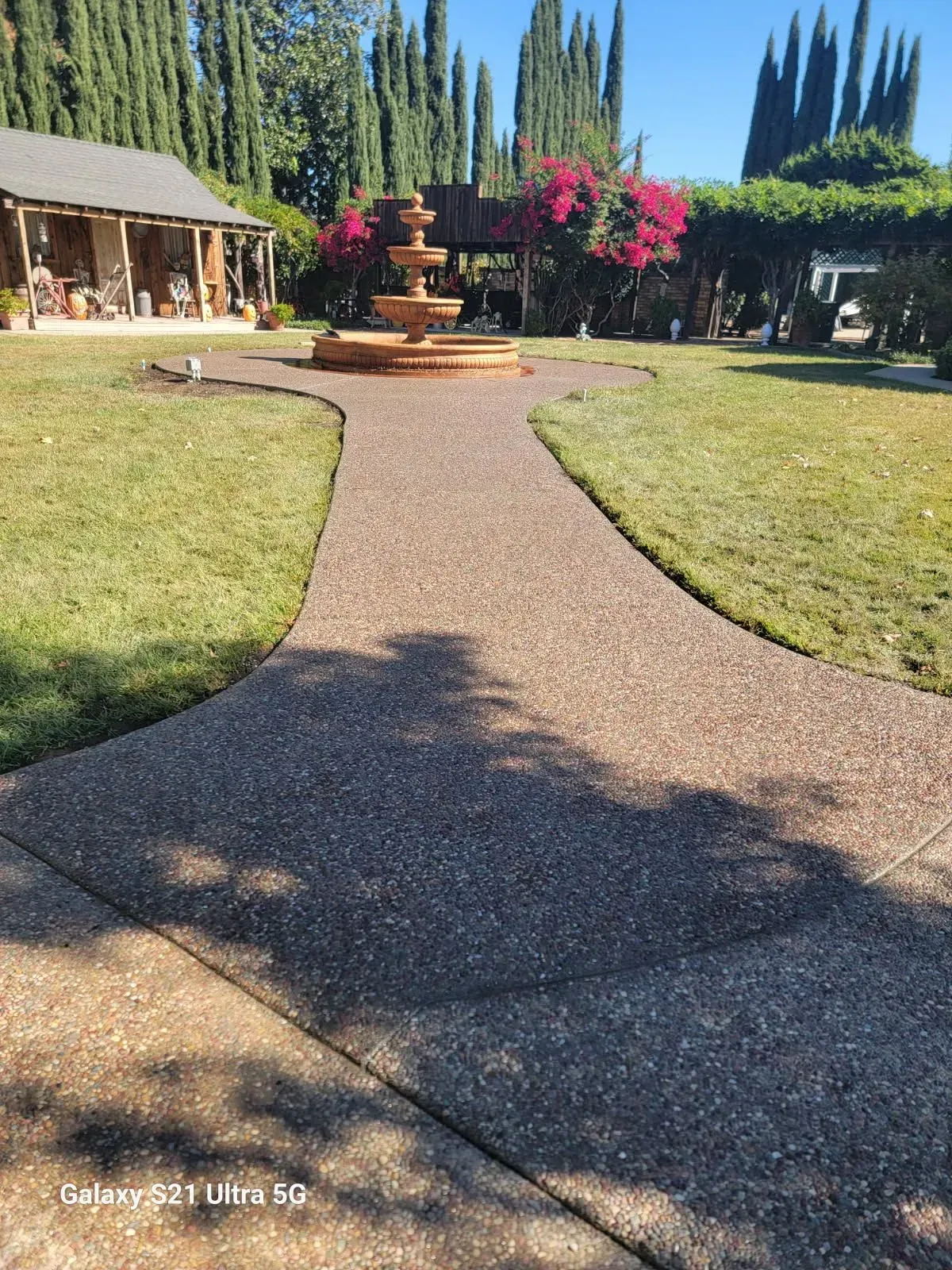 A concrete walkway leading to a fountain in front of a house.