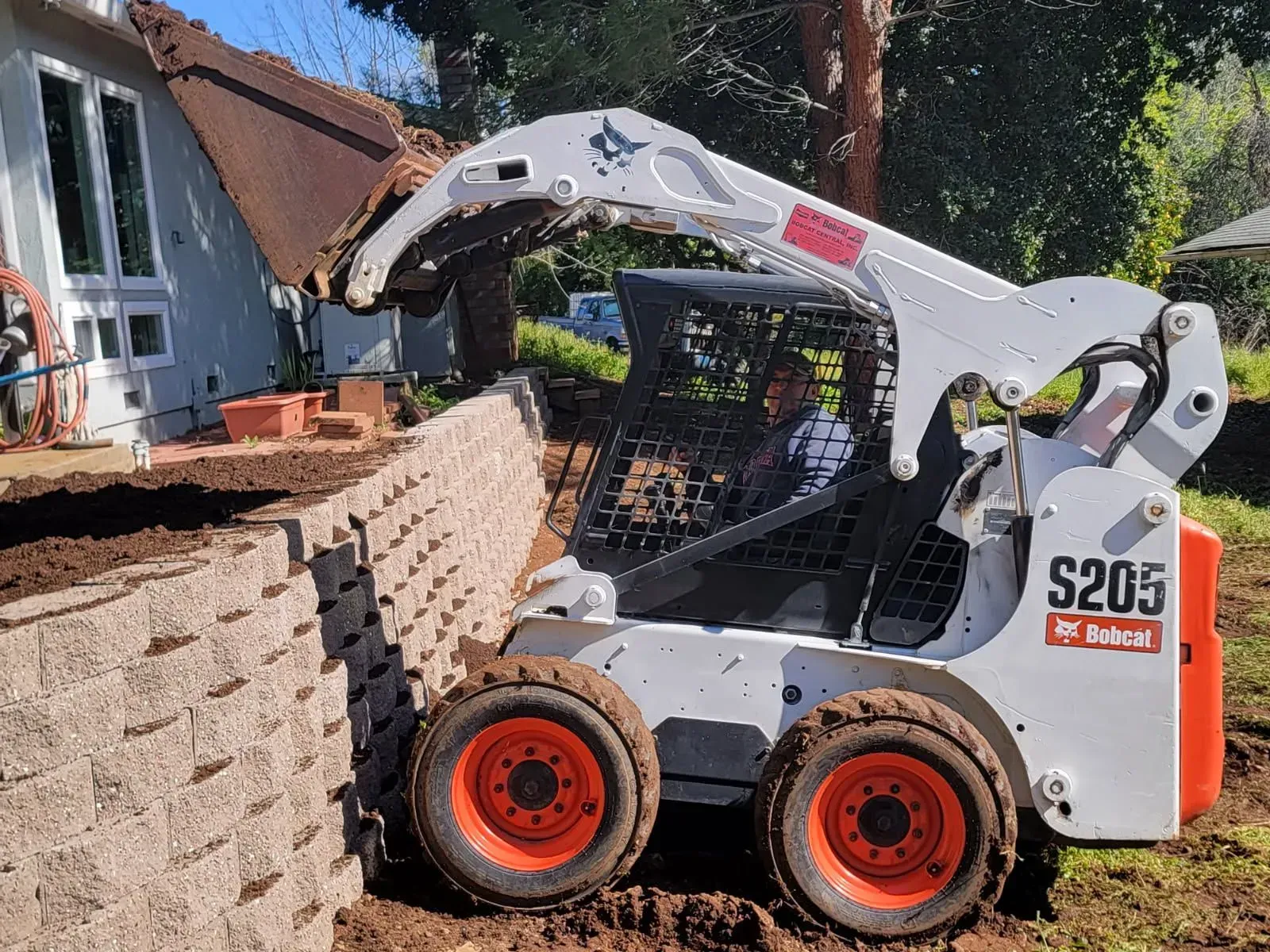A bobcat s205 is loading dirt into a bucket in front of a house.