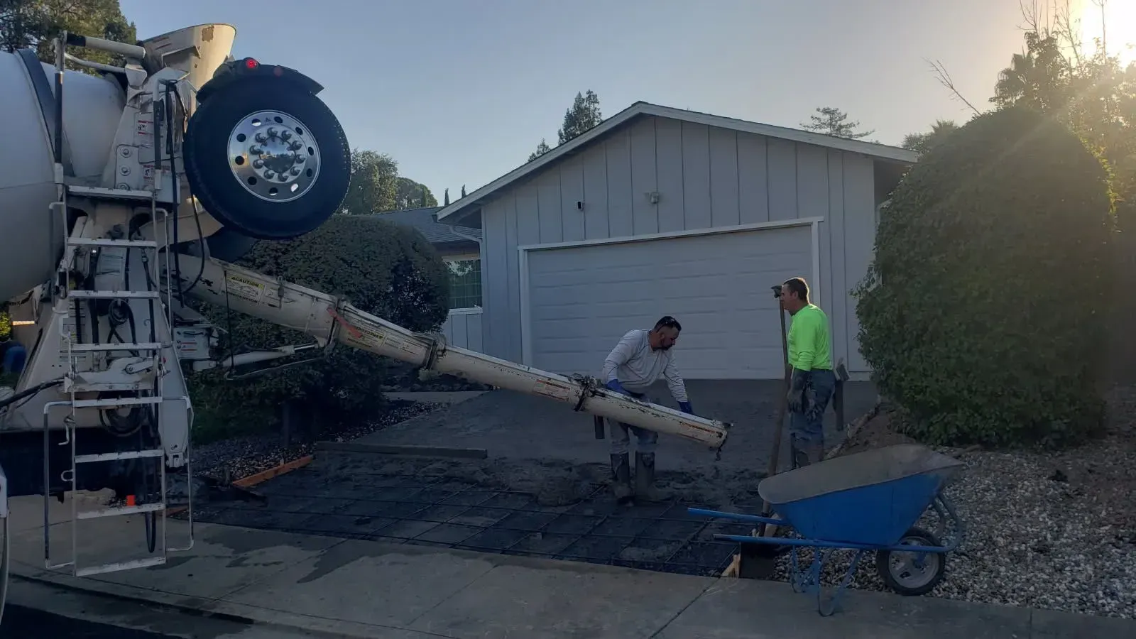 A concrete truck is pouring concrete into a driveway in front of a garage.