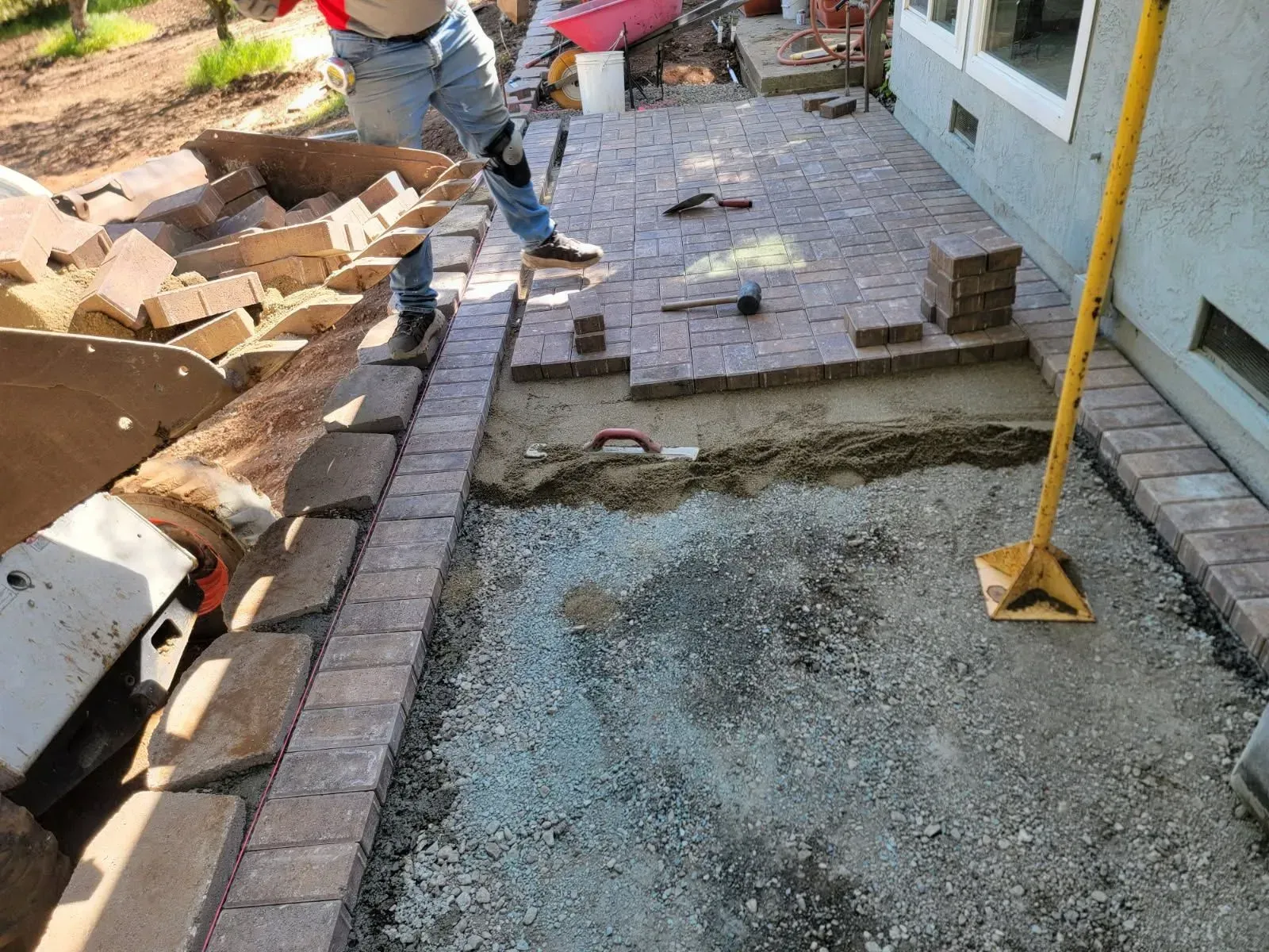 A man is laying bricks on a sidewalk in front of a house.