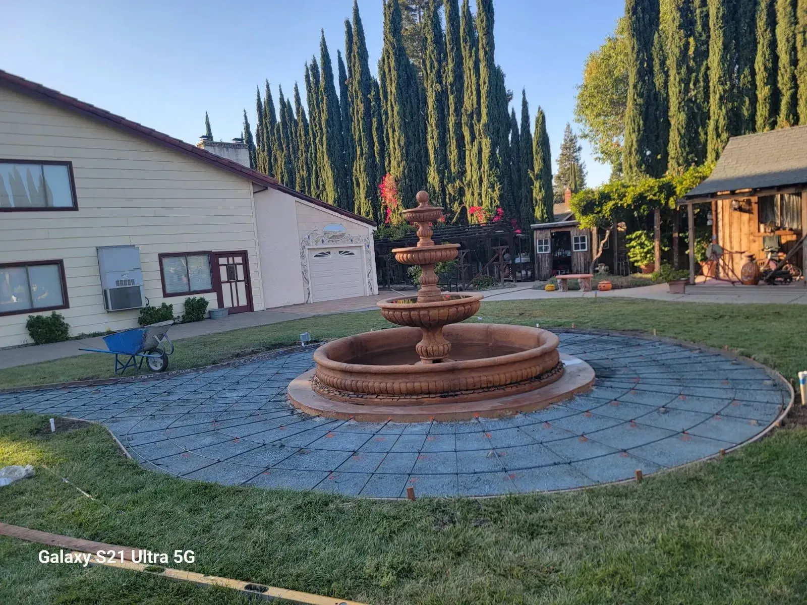 A large fountain is in the middle of a lush green yard in front of a house.