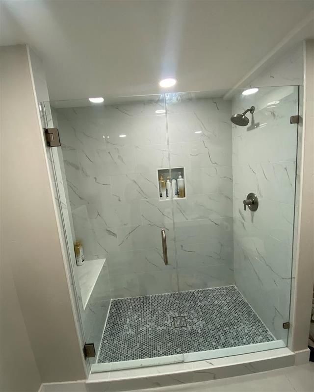 Modern, marble-tiled shower with glass doors, a built-in shelf, and a mosaic tile floor.