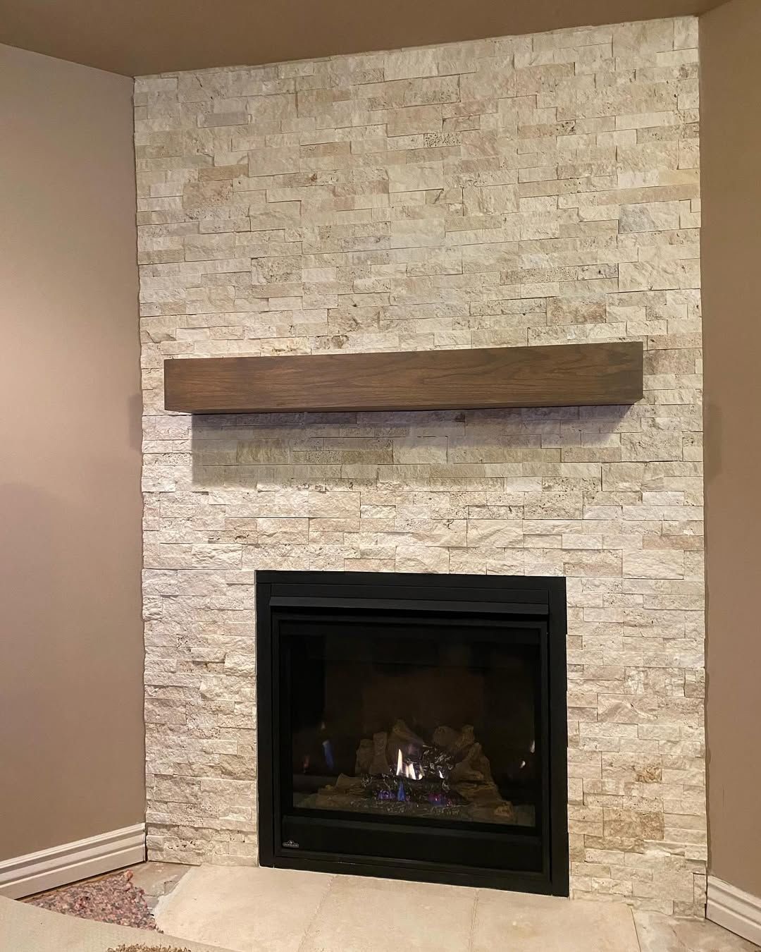 Fireplace with a stone veneer, black insert, and wooden mantel.
