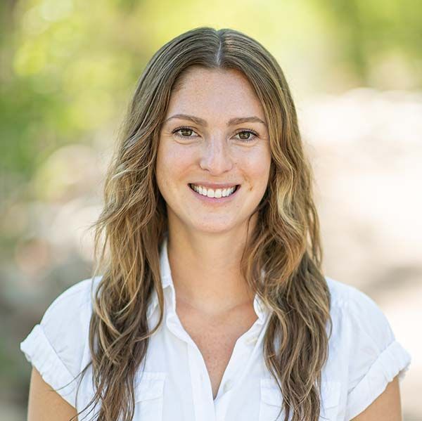 A woman with long hair is smiling for the camera while wearing a white shirt.