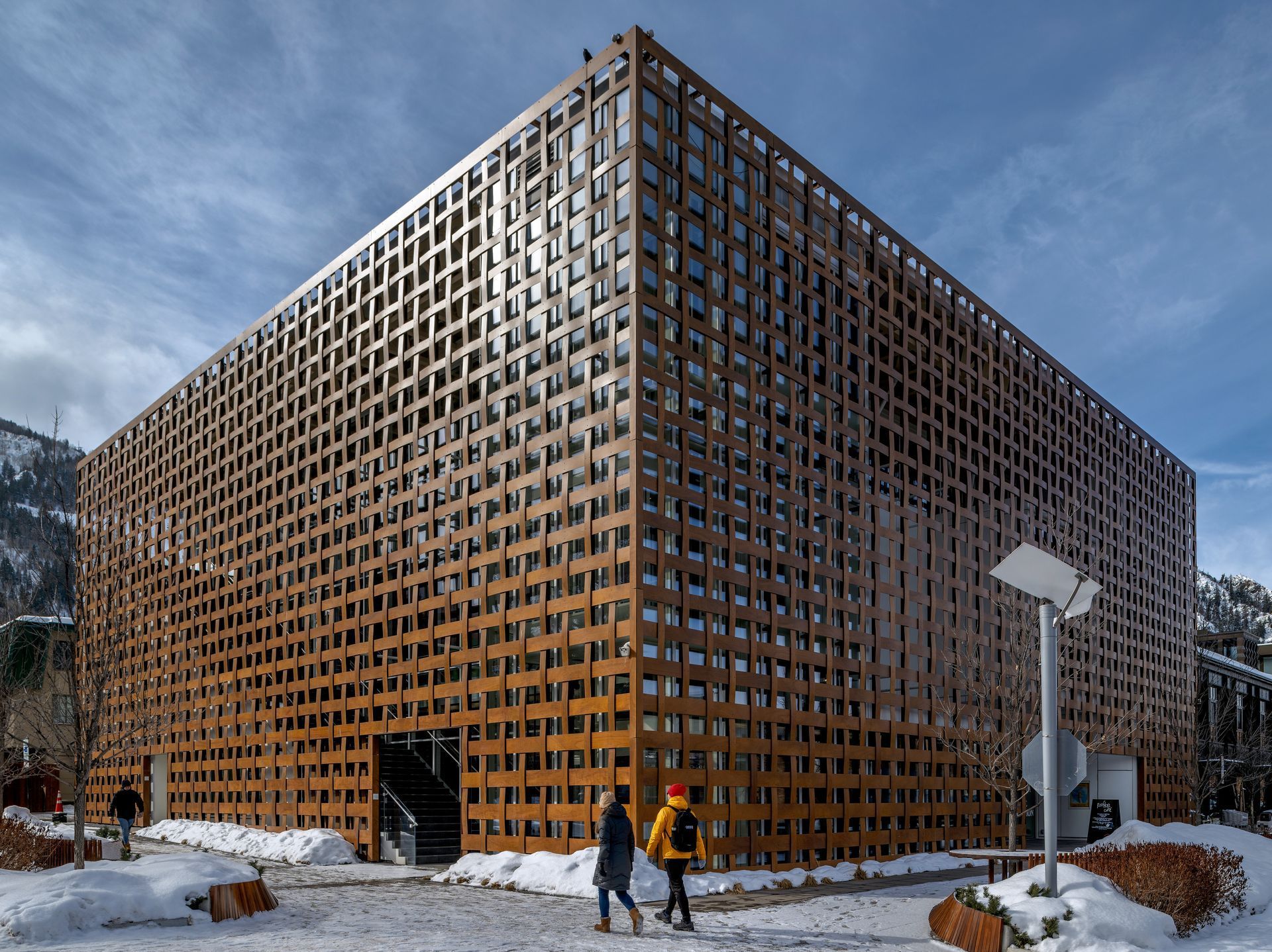 A couple of people are walking in front of a large wooden building in the snow.