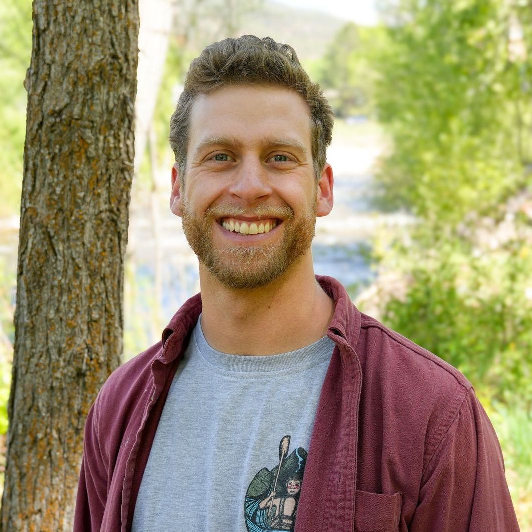 A man with blonde hair wearing a red shirt smiles for the camera