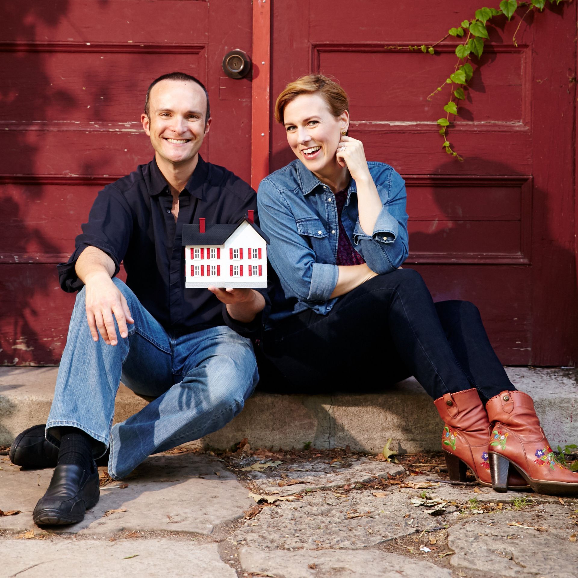 A man and a woman sit on steps holding a small house