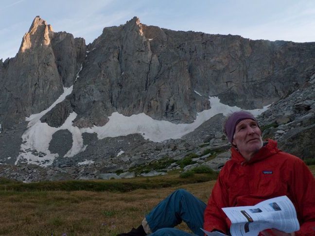 Randy Udall, a man wearing a winter cap and a red coat, sits in front of a mountain range.