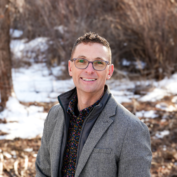 A man wearing glasses and a suit is standing in the snow.