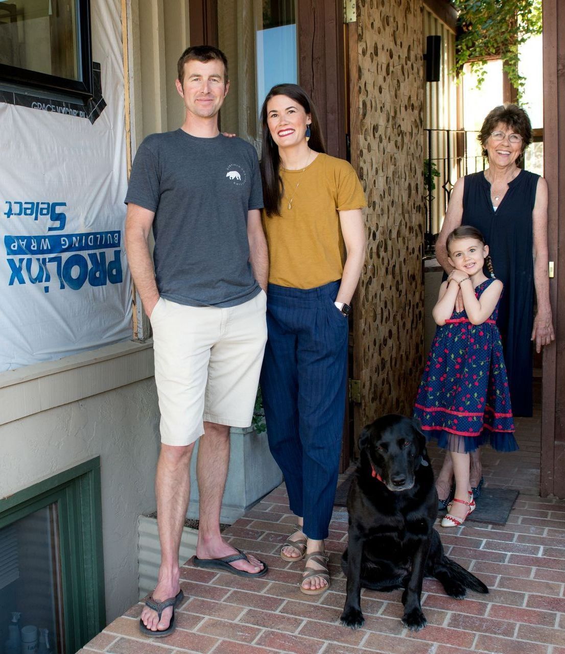 A family standing on a porch with a black dog