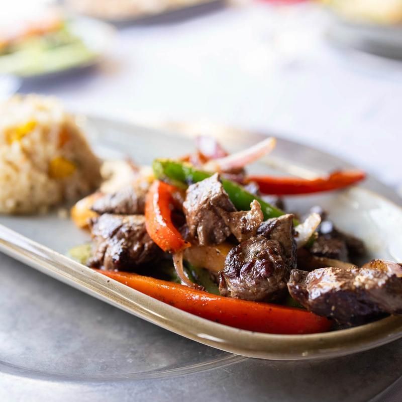 Plated beef stir-fry with red peppers and onions, served beside rice on a white dish