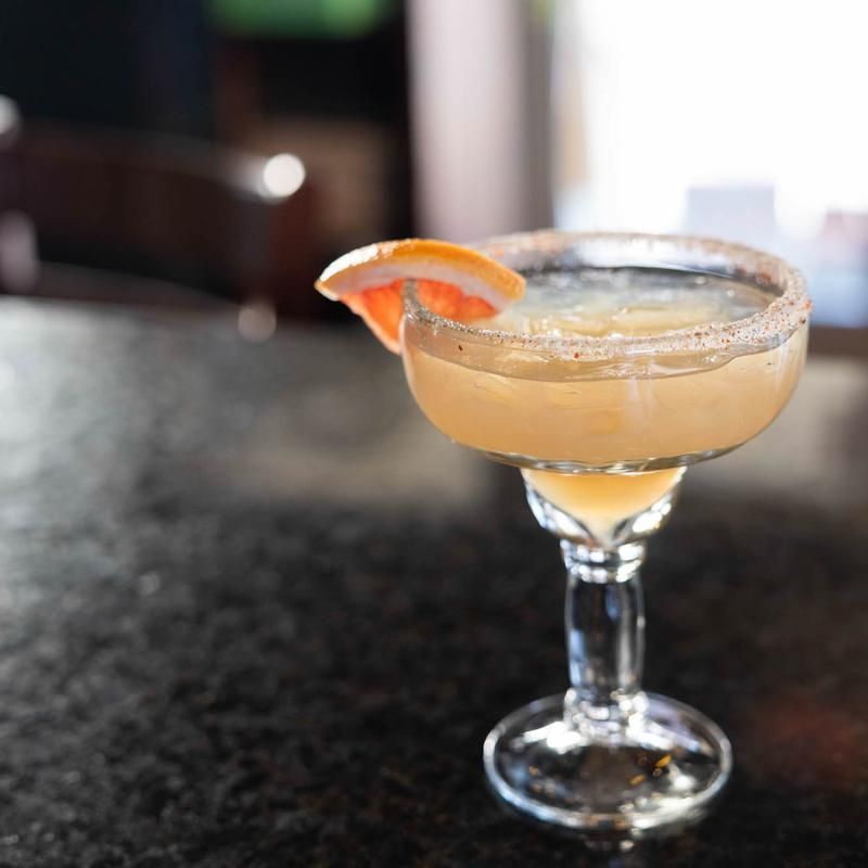 Cocktail in a coupe glass with a grapefruit garnish on a dark bar countertop