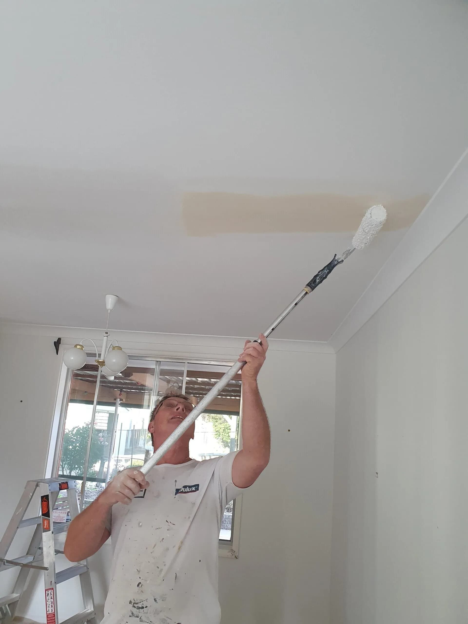 A Man Is Painting The Ceiling With A Ladder In The Background — Peter the Painter In Evatt, ACT