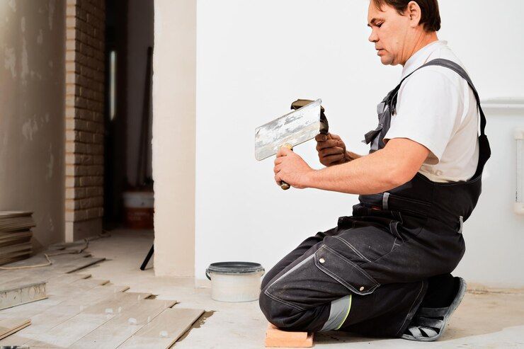 A Man Kneeling Down Holding A Spatula And A Hammer — Peter the Painter In Evatt, ACT