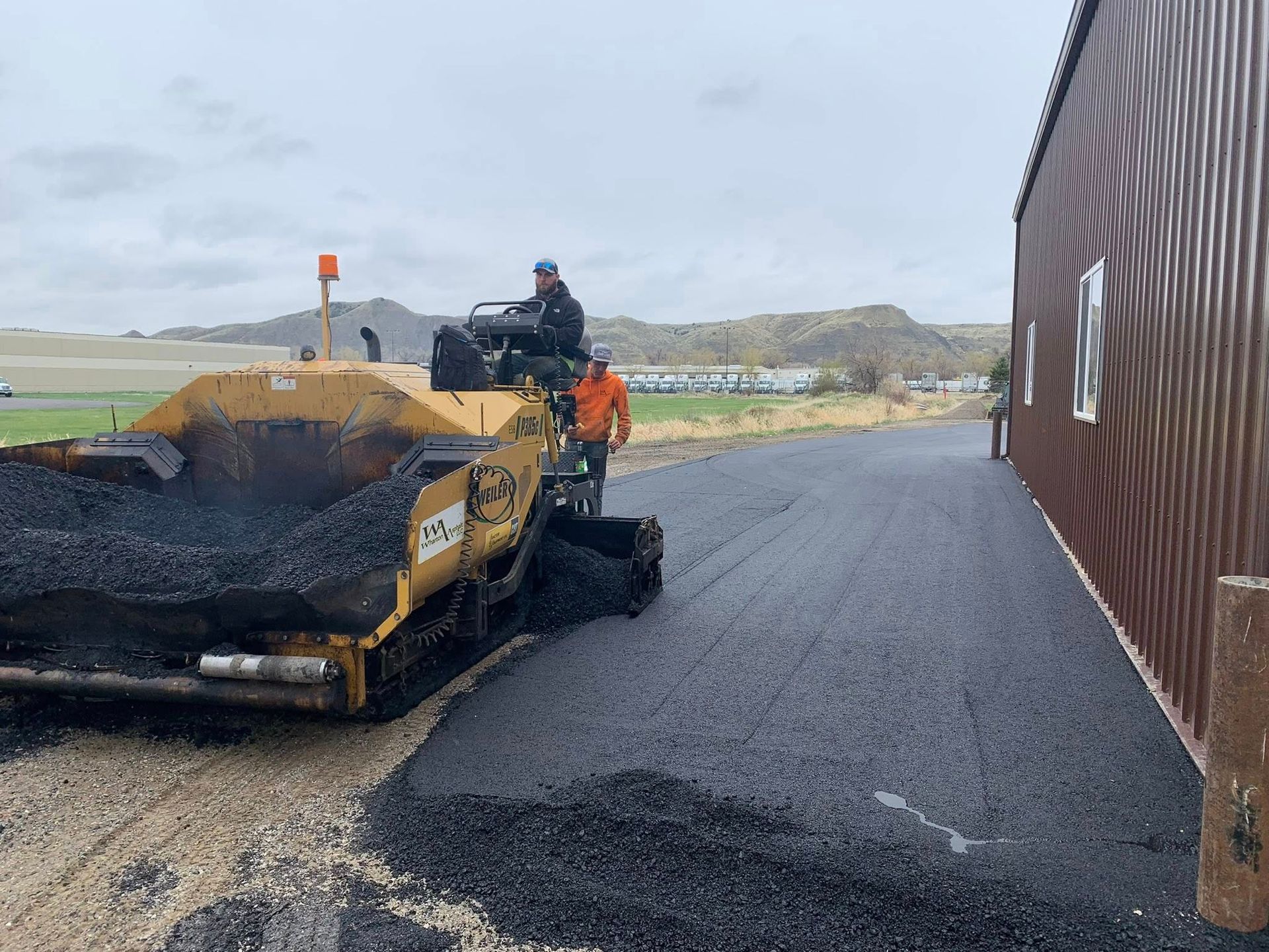 A man is driving a bulldozer on a road next to a building.