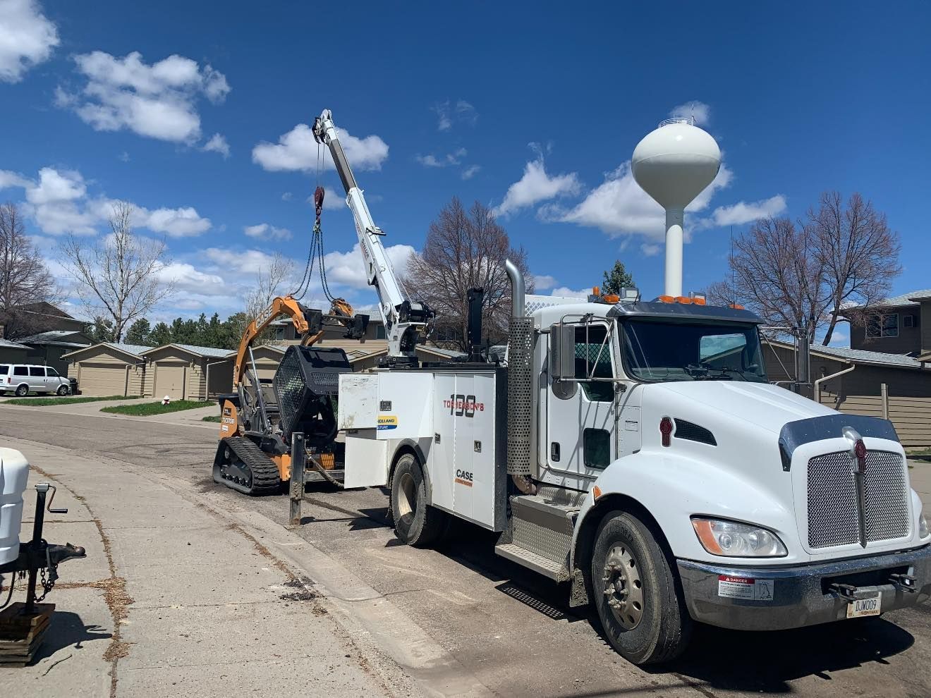 A white tow truck with a crane attached to it is parked on the side of the road.