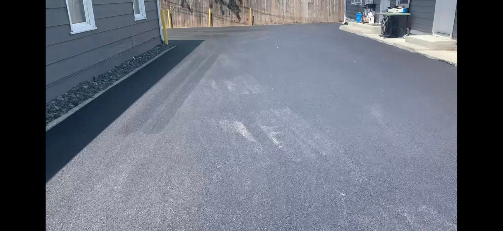 A black asphalt driveway with a house in the background.