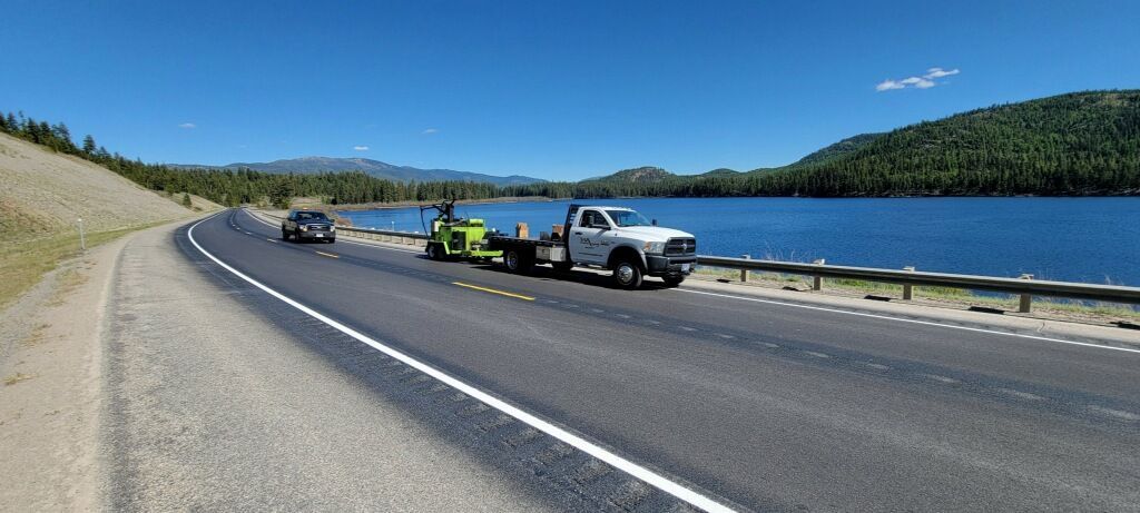 A tow truck is towing a car on a highway next to a lake.