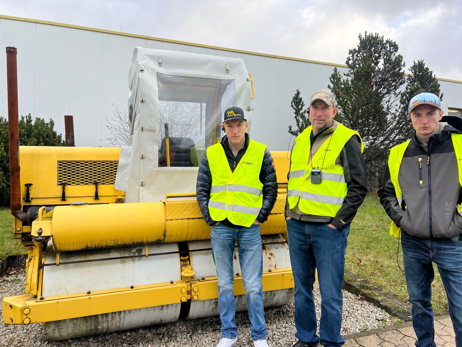 Three men in yellow vests are standing in front of a yellow tractor.